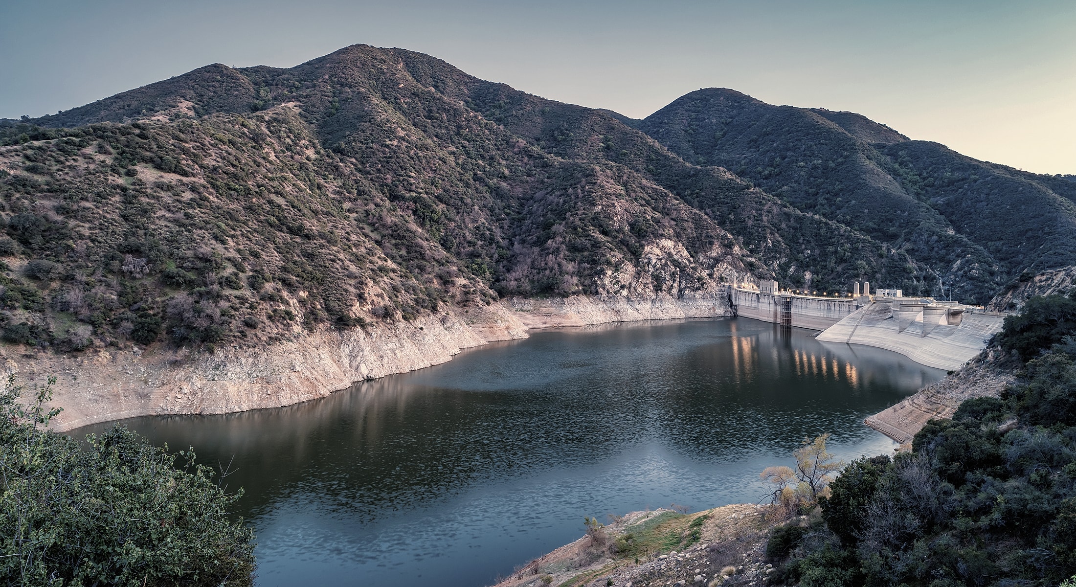 Reservoir surrounded by mountains at sunset.